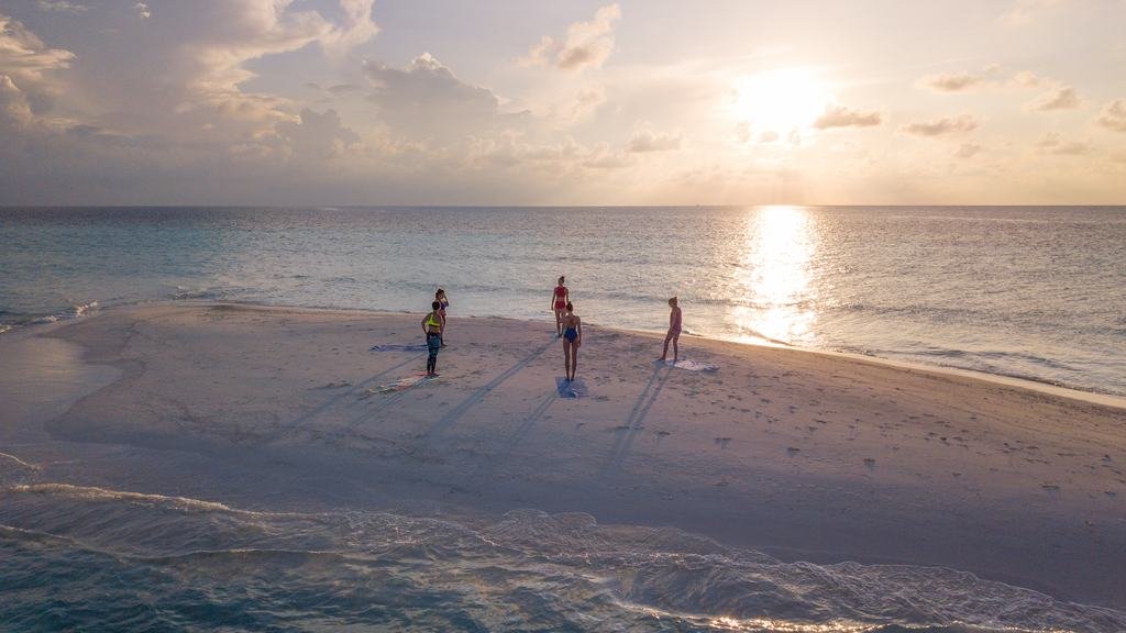 Three people standing on a sandbank at sunset, the sun low over flat water.
