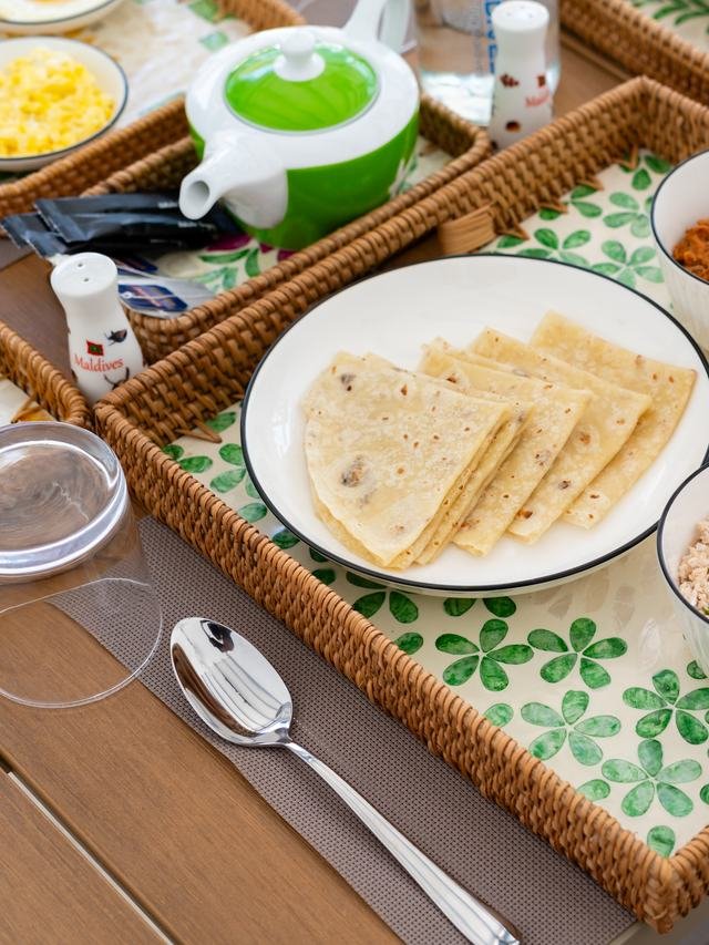 A breakfast tray: flatbread, curry, mashuni, fruit and coffee.
