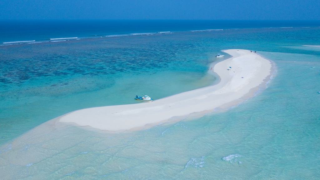 A narrow sandbank curving into pale shallows, with two small boats moored against it.