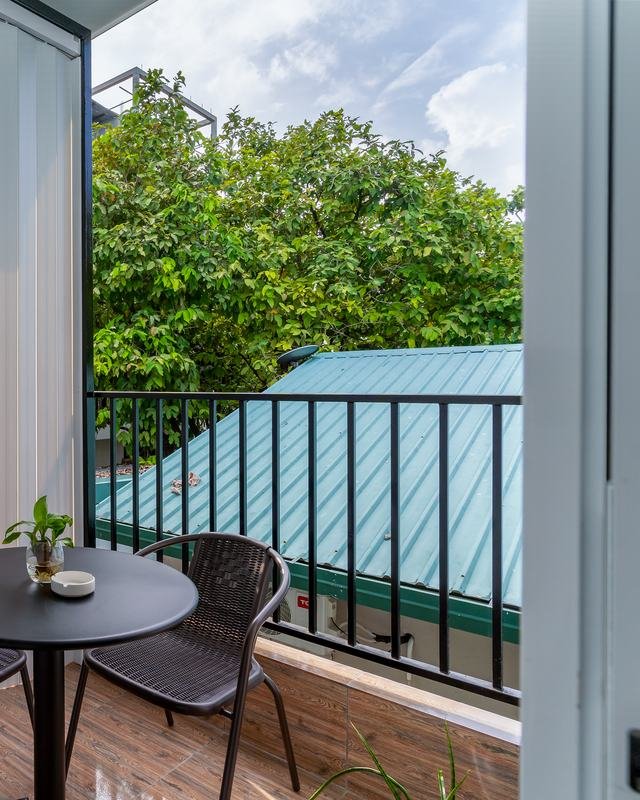 The private balcony: a small table and two chairs, with treetops and a neighbouring roof beyond the railing.