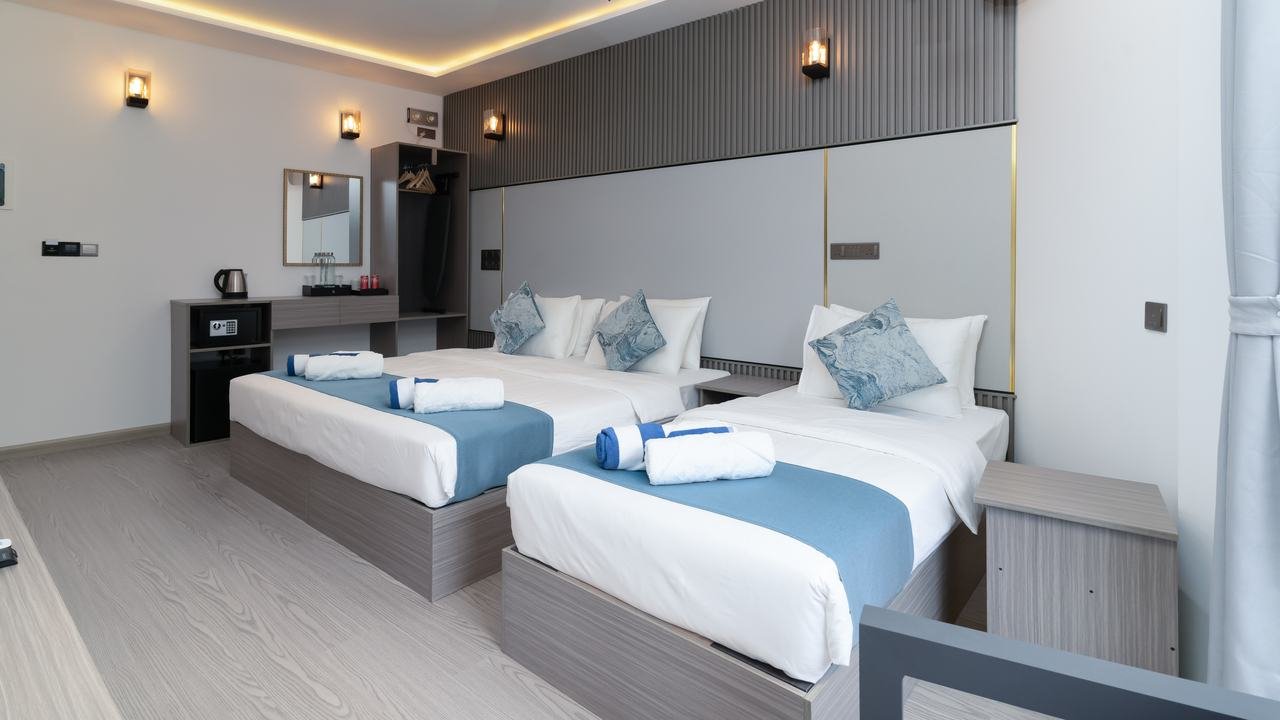 The room seen wide: twin beds turned down, a desk with a kettle and mirror, and warm lighting along the ceiling.