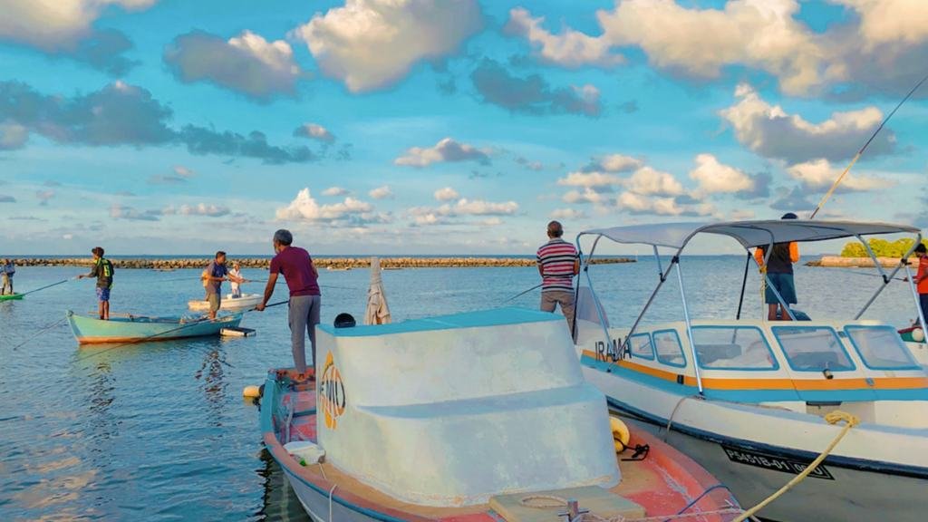 Ukulhas harbour at dusk: local boats moored against the breakwater, men working on deck.